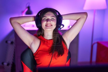 Téléchargez les photos : Jeune femme caucasienne streamer souriant confiant détendu avec les mains sur la tête à la salle de jeu - en image libre de droit