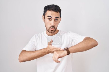 Téléchargez les photos : Handsome hispanic man standing over white background in hurry pointing to watch time, impatience, upset and angry for deadline delay - en image libre de droit