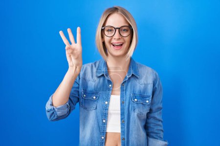 Téléchargez les photos : Young caucasian woman standing over blue background showing and pointing up with fingers number three while smiling confident and happy. - en image libre de droit