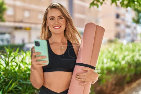 Photo for Young woman using smartphone holding yoga mat at park - Royalty Free Image