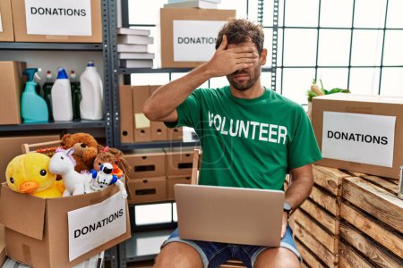 Photo for Young handsome man wearing volunteer t shirt using laptop covering eyes with hand, looking serious and sad. sightless, hiding and rejection concept - Royalty Free Image