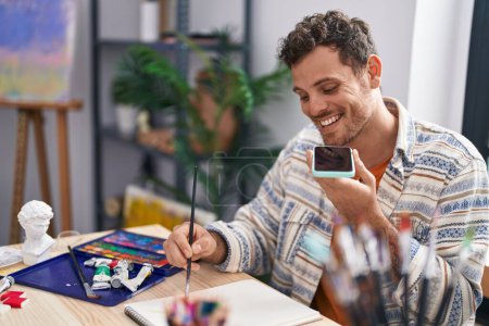 Photo for Young hispanic man artist talking on the smartphone drawing at art studio - Royalty Free Image
