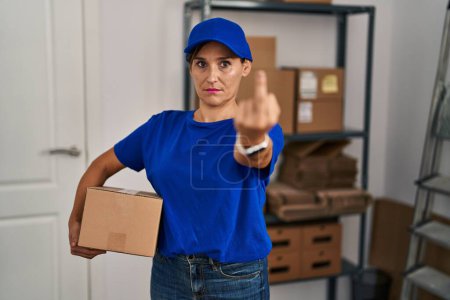 Foto de Middle age brunette woman working wearing delivery uniform and cap showing middle finger, impolite and rude fuck off expression - Imagen libre de derechos