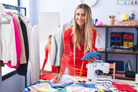 Téléchargez les photos : Jeune femme blonde tailleur à l'aide de dessin tactile conception de vêtements au magasin de tailleur - en image libre de droit