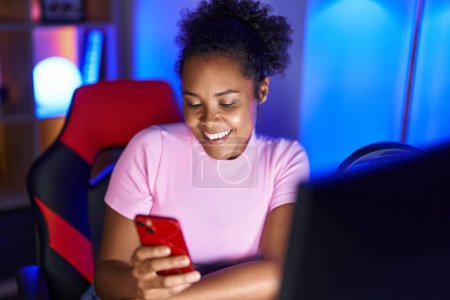 Foto de Transmisor de mujer afroamericana usando computadora y teléfono inteligente en la sala de juegos - Imagen libre de derechos