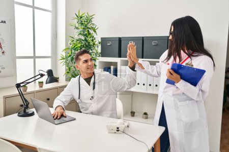 Photo for Man and woman wearing doctor uniform high five with hands raised up at clinic - Royalty Free Image