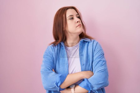 Téléchargez les photos : Young hispanic woman with red hair standing over pink background looking to the side with arms crossed convinced and confident - en image libre de droit