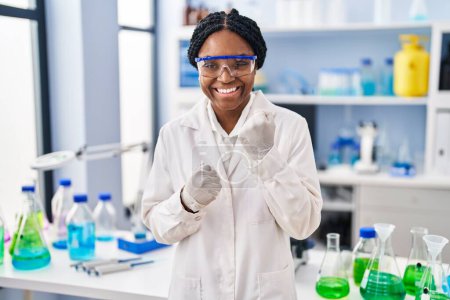 Foto de Mujer afroamericana trabajando en laboratorio científico celebrando sorprendida y sorprendida por el éxito con los brazos levantados y los ojos cerrados - Imagen libre de derechos