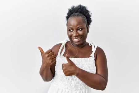 Téléchargez les photos : Jeune femme africaine debout sur fond blanc isolé pointant le dos derrière avec la main et les pouces levés, souriant confiant - en image libre de droit