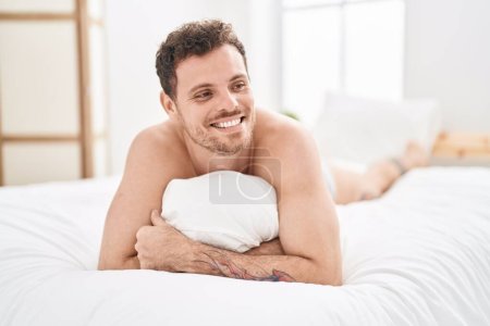 Téléchargez les photos : Jeune homme hispanique étreignant oreiller couché sur le lit dans la chambre - en image libre de droit