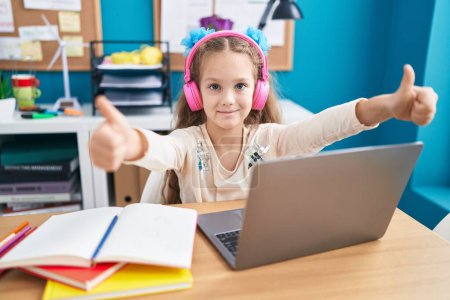 Téléchargez les photos : Adorable caucasian girl student listening music doing ok gesture with thumbs up at office - en image libre de droit