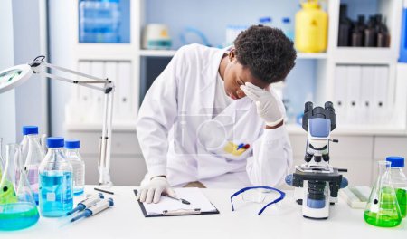Foto de African american woman wearing scientist uniform stressed working at laboratory - Imagen libre de derechos