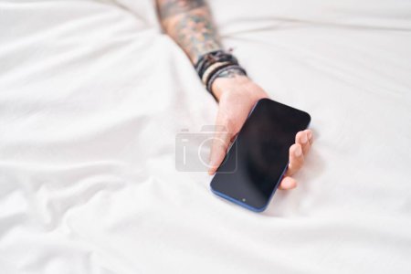 Photo for Young hispanic man lying on bed holding smartphone at bedroom - Royalty Free Image