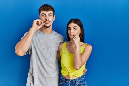 Photo for Young hispanic couple standing together over blue background mouth and lips shut as zip with fingers. secret and silent, taboo talking - Royalty Free Image
