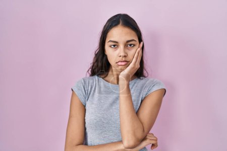 Téléchargez les photos : Jeune femme brésilienne portant t-shirt décontracté sur fond rose pensant fatigué et ennuyé avec des problèmes de dépression avec les bras croisés. - en image libre de droit