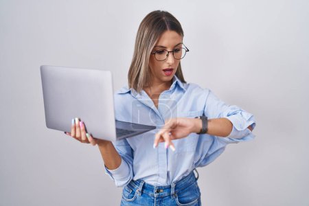 Téléchargez les photos : Jeune femme travaillant à l'aide d'un ordinateur portable en regardant le temps de la montre inquiet, peur d'arriver en retard - en image libre de droit