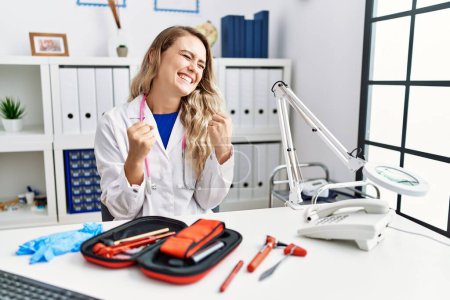Photo for Young beautiful doctor woman with reflex hammer and medical instruments very happy and excited doing winner gesture with arms raised, smiling and screaming for success. celebration concept. - Royalty Free Image