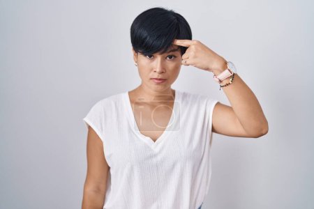 Téléchargez les photos : Jeune femme asiatique avec les cheveux courts debout sur fond isolé pointant malheureux de boutons sur le front, infection laide de la tête noire. acné et problème de peau - en image libre de droit
