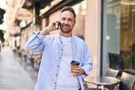 Photo for Young caucasian man talking on the smartphone drinking coffee at coffee shop terrace - Royalty Free Image