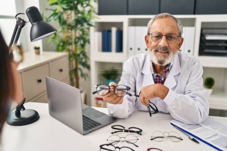 Foto de Hombre mayor de pelo gris óptico sosteniendo gafas mostrando al paciente en la clínica - Imagen libre de derechos