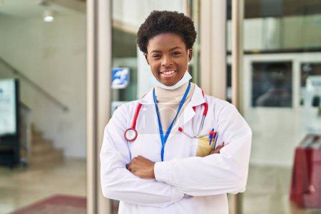 Foto de Mujer afroamericana vistiendo uniforme médico y máscara médica de pie con los brazos cruzados gesto en la calle - Imagen libre de derechos
