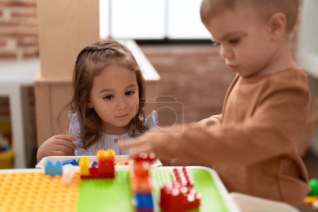 Foto de Adorable chica y niño jugando con piezas de bloques de construcción sentado en la mesa en el jardín de infantes - Imagen libre de derechos