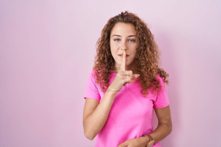 Foto de Young caucasian woman standing over pink background asking to be quiet with finger on lips. silence and secret concept. - Imagen libre de derechos