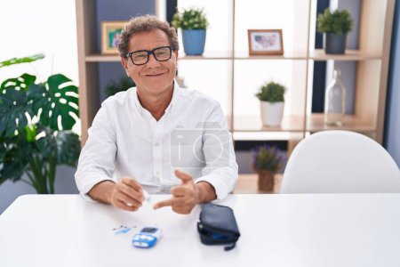 Foto de Hombre de mediana edad sonriendo confiado midiendo glucosa en casa - Imagen libre de derechos