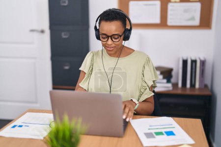 Téléchargez les photos : Femme afro-américaine travailleur d'affaires en utilisant un ordinateur portable et écouteurs travaillant au bureau - en image libre de droit