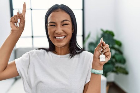 Photo for Young hispanic woman holding keys of new home smiling amazed and surprised and pointing up with fingers and raised arms. - Royalty Free Image