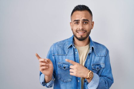 Téléchargez les photos : Young hispanic man standing over isolated background pointing aside worried and nervous with both hands, concerned and surprised expression - en image libre de droit
