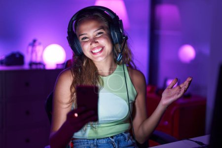 Foto de Young hispanic woman playing video games with smartphone celebrating achievement with happy smile and winner expression with raised hand - Imagen libre de derechos