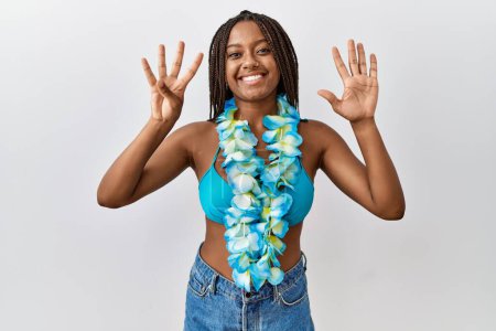 Téléchargez les photos : Jeune femme afro-américaine avec des tresses en bikini et lei hawaïen montrant et pointant vers le haut avec les doigts numéro neuf tout en souriant confiant et heureux. - en image libre de droit