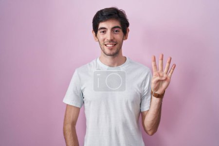 Téléchargez les photos : Jeune homme hispanique debout sur fond rose montrant et pointant vers le haut avec les doigts numéro quatre tout en souriant confiant et heureux. - en image libre de droit