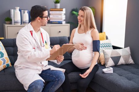Téléchargez les photos : Homme et femme médecin et patiente enceinte ayant une consultation médicale à l'aide d'un tensiomètre à domicile - en image libre de droit