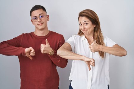 Photo for Mother and son standing together over isolated background doing thumbs up and down, disagreement and agreement expression. crazy conflict - Royalty Free Image
