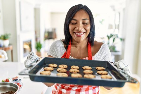 Photo for Hispanic brunette woman holding tray with homemade cookies at the kitchen - Royalty Free Image