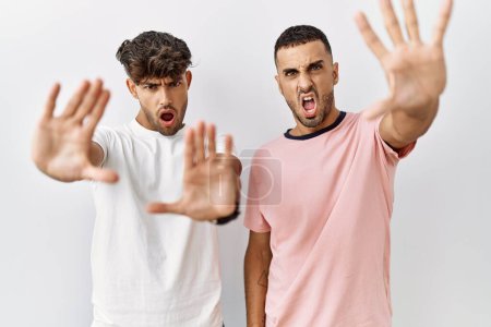 Téléchargez les photos : Jeune couple gay debout sur fond isolé faire arrêter geste avec les mains paumes, expression de colère et de frustration - en image libre de droit
