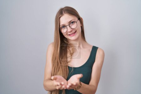Téléchargez les photos : Jeune femme caucasienne debout sur fond blanc souriant avec les mains paumes ensemble recevant ou donnant geste. maintien et protection - en image libre de droit
