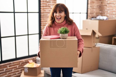 Photo for Middle age hispanic woman moving to a new home holding cardboard box smiling and laughing hard out loud because funny crazy joke. - Royalty Free Image