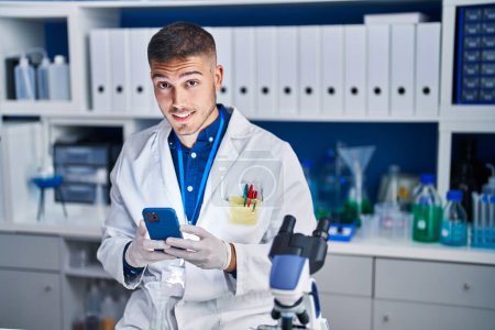 Téléchargez les photos : Young hispanic man scientist using smartphone at laboratory - en image libre de droit