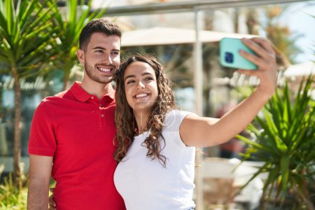 Foto de Joven pareja hispana sonriendo confiada hacer selfie por el teléfono inteligente en la calle - Imagen libre de derechos