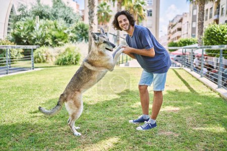 Photo for Young man smiling confident playing with dog at park - Royalty Free Image