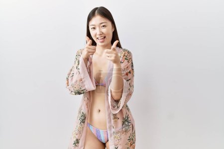 Photo for Young asian woman wearing bikini an floral kimono pointing fingers to camera with happy and funny face. good energy and vibes. - Royalty Free Image