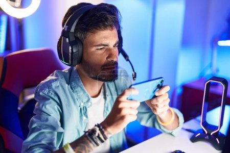Photo for Young hispanic man streamer playing video game using smartphone at gaming room - Royalty Free Image