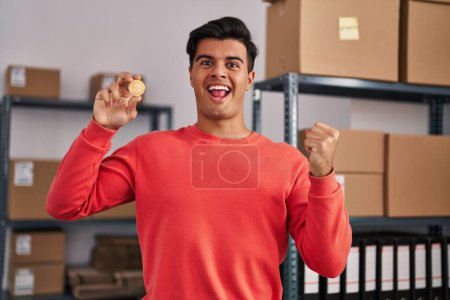 Photo for Hispanic man working at small business ecommerce holding bitcoin screaming proud, celebrating victory and success very excited with raised arms - Royalty Free Image