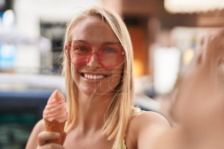 Foto de Mujer rubia joven con gafas de sol de corazón hacen selfie por la cámara en la calle - Imagen libre de derechos