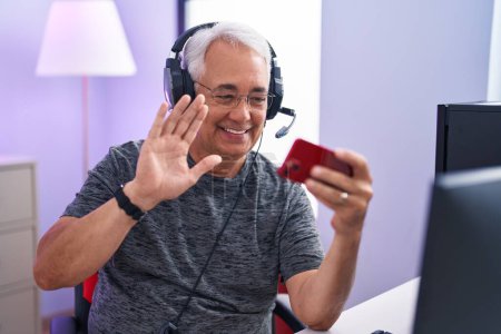 Téléchargez les photos : Homme du Moyen Âge avec les cheveux gris jouer à des jeux vidéo avec smartphone regardant positif et heureux debout et souriant avec un sourire confiant montrant les dents - en image libre de droit