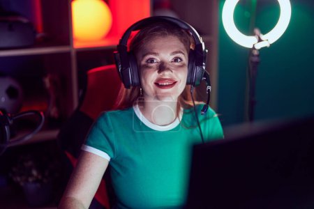 Photo for Young redhead woman streamer smiling confident sitting on table at gaming room - Royalty Free Image
