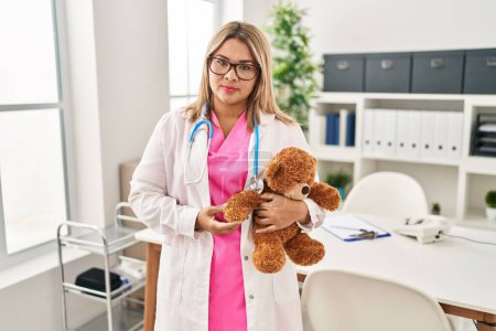 Photo for Young hispanic doctor woman holding teddy bear thinking attitude and sober expression looking self confident - Royalty Free Image